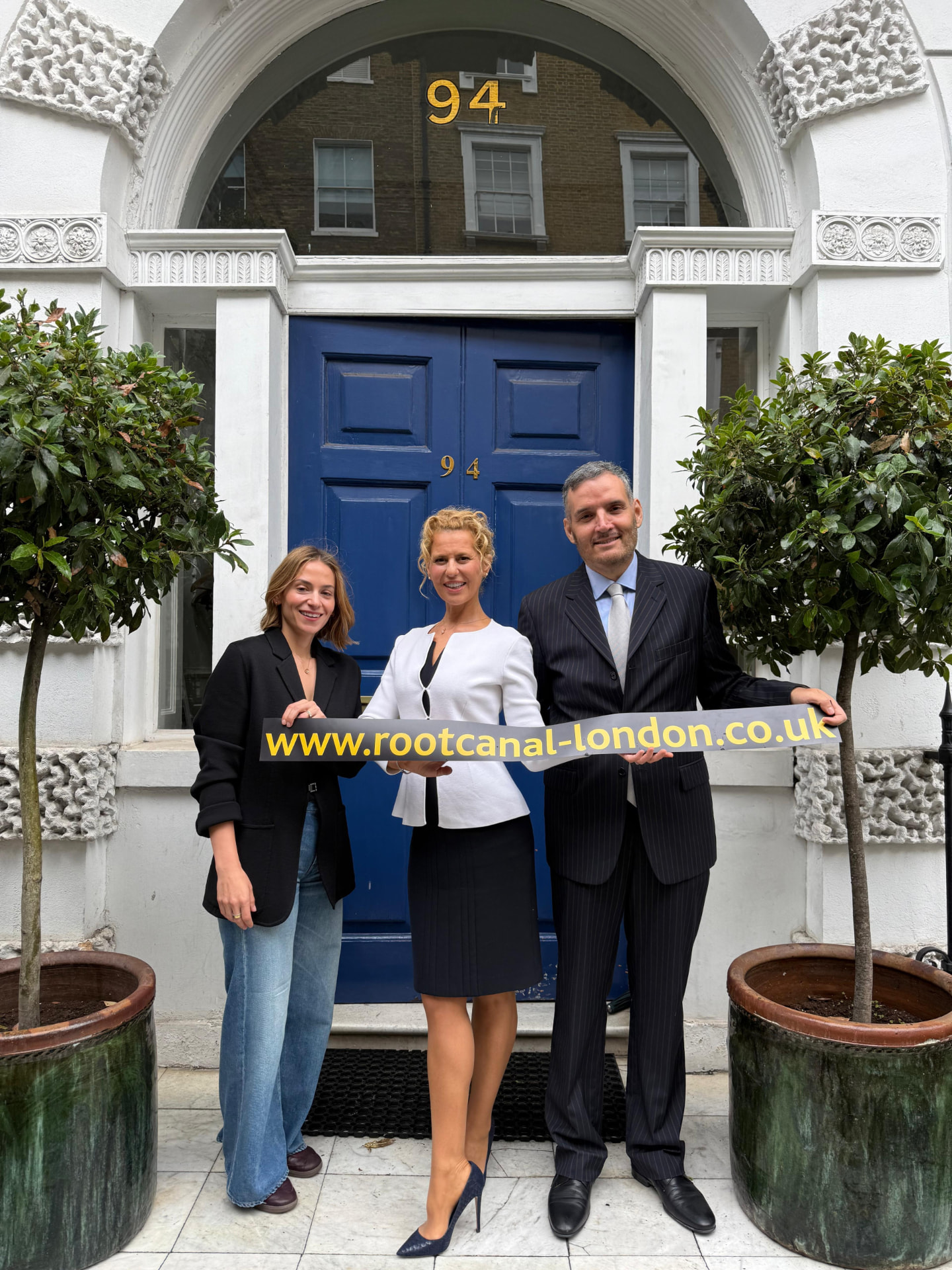 The blue front door of number 94 Harley Street, with three members of the team outside holding the practice sign